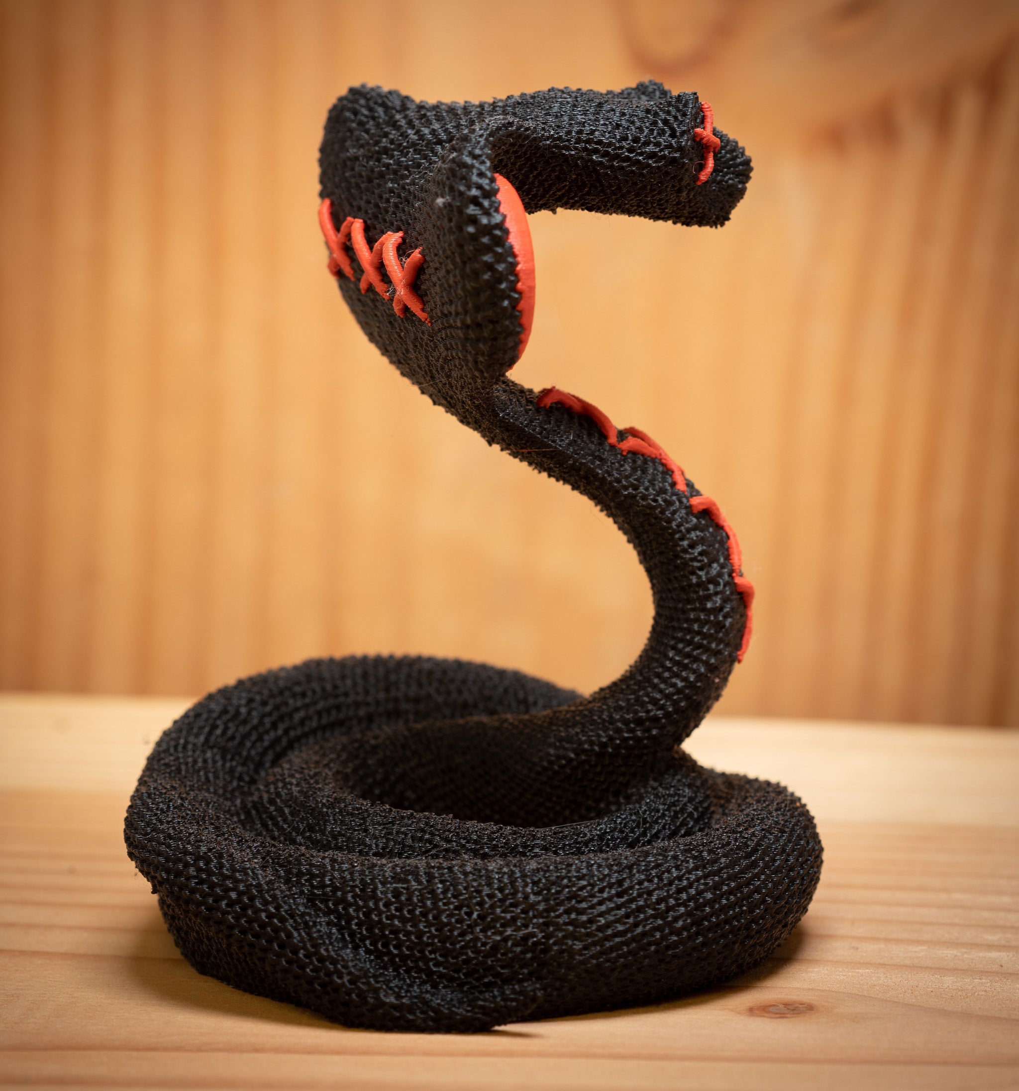 MM Figur Sacky Serpent (13 cm) er en sort, sammenrullet voodoo-slangefigur med røde syninger, der står oprejst på en træplade - perfekt som hyldeudsmykning.