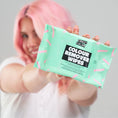Load image into Gallery viewer, En person med pastelfarvet hår smiler og holder en turkis Crazy Color Color Remover Wipes/Farvefjerner-pakke op mod kameraet. Disse biologisk nedbrydelige klude fjerner skånsomt hårfarve; emballagen har pink og hvide detaljer på en lys baggrund.
